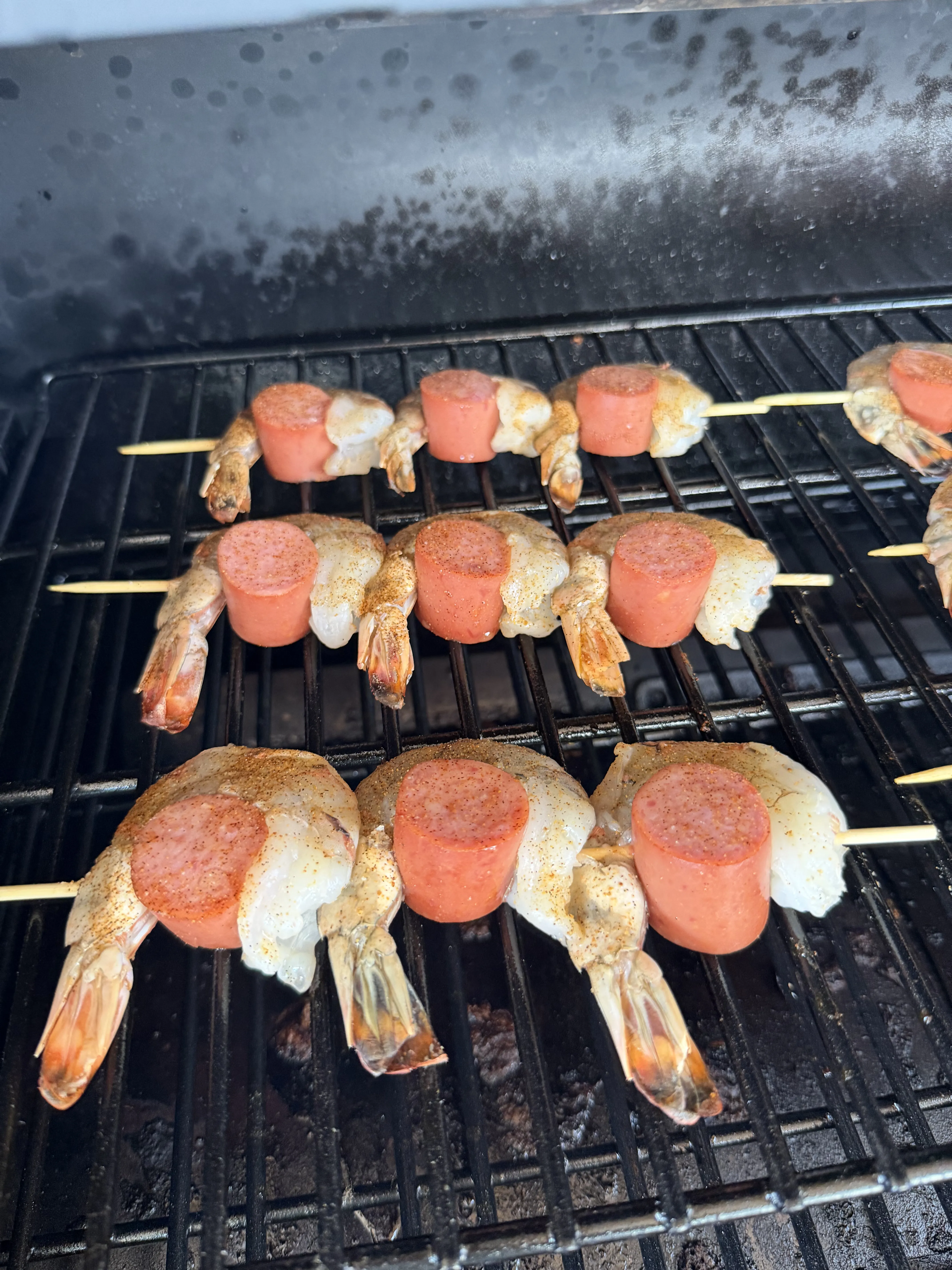 Seasoned smoked shrimp and sausage skewers cooking on a dark grill grate, threaded on bamboo skewers