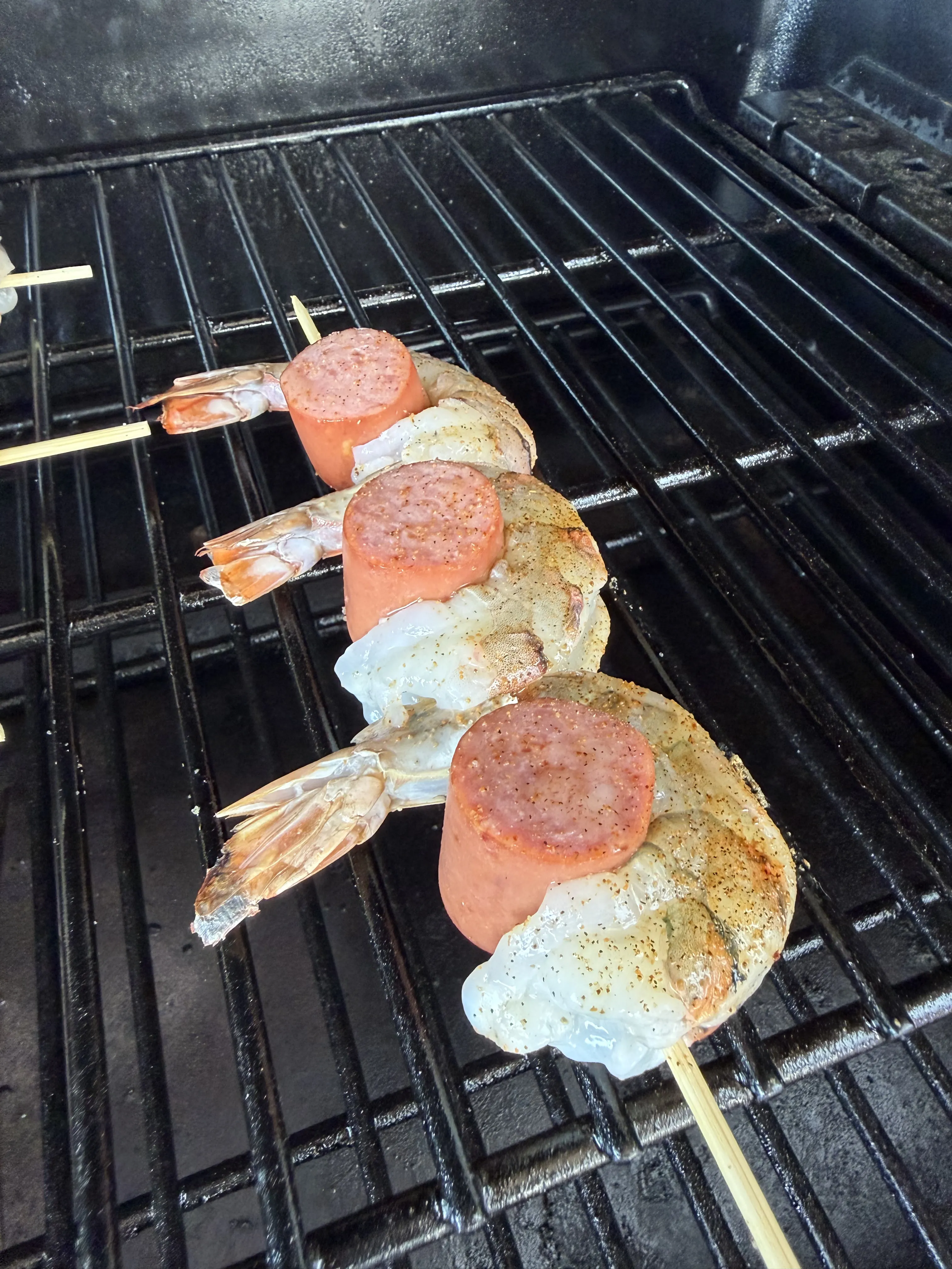 Shrimp and sliced sausage skewers on wooden skewers cooking on a dark grill grate