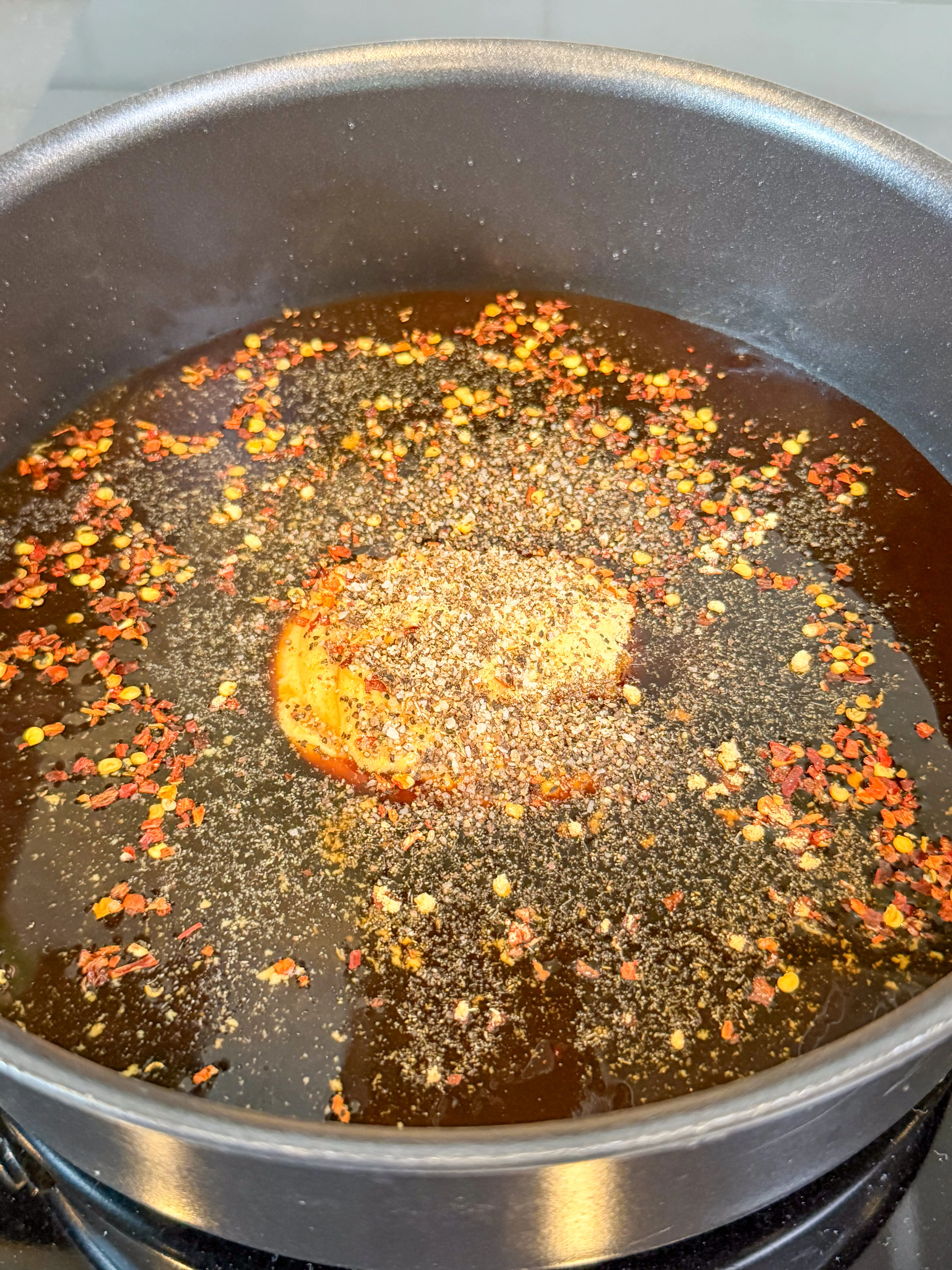 Dark molasses glaze with red pepper flakes and black pepper simmering in a nonstick pan on stovetop
