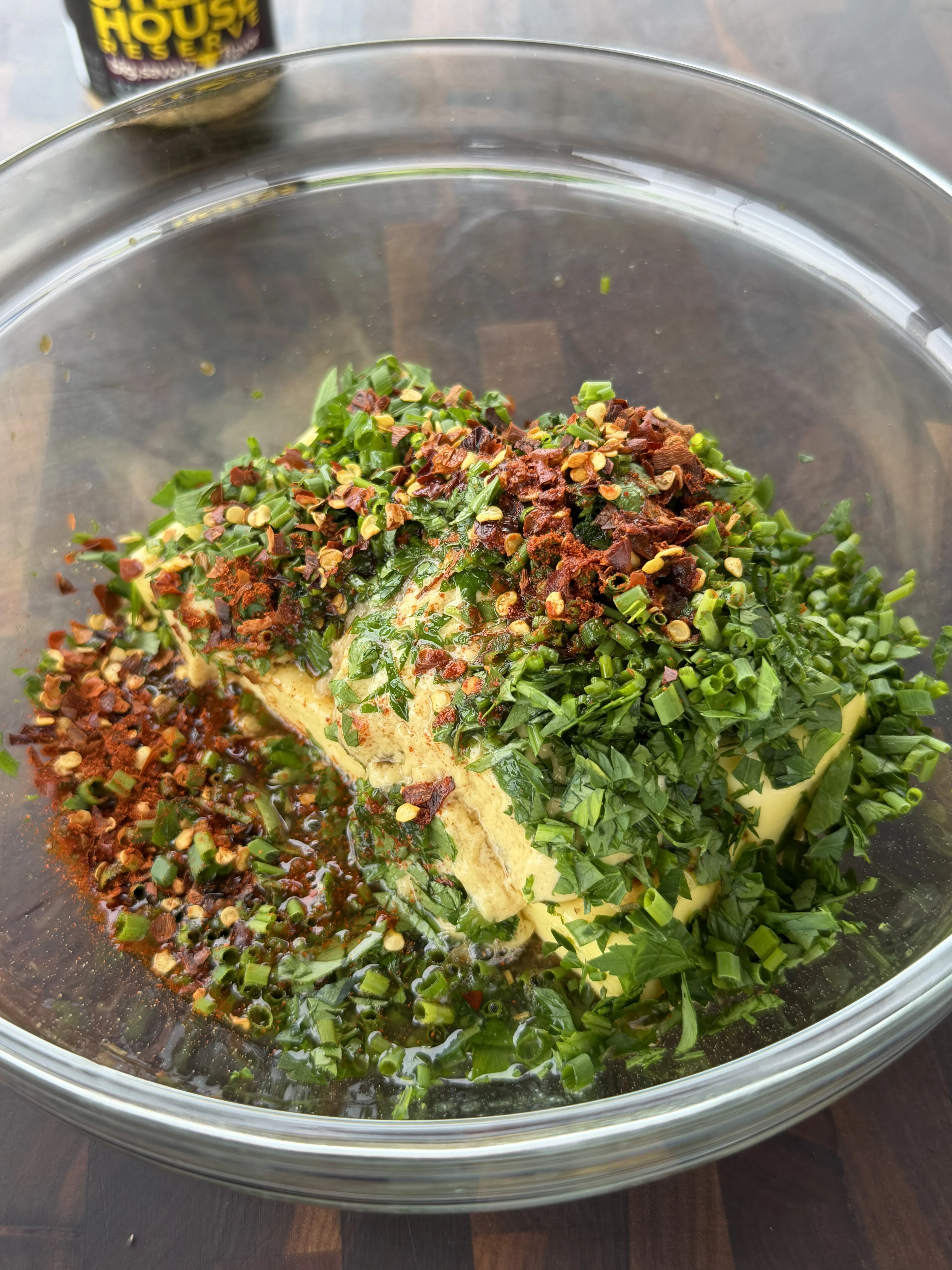 Softened butter with chopped herbs, scallions, chili flakes, and spices in a glass bowl