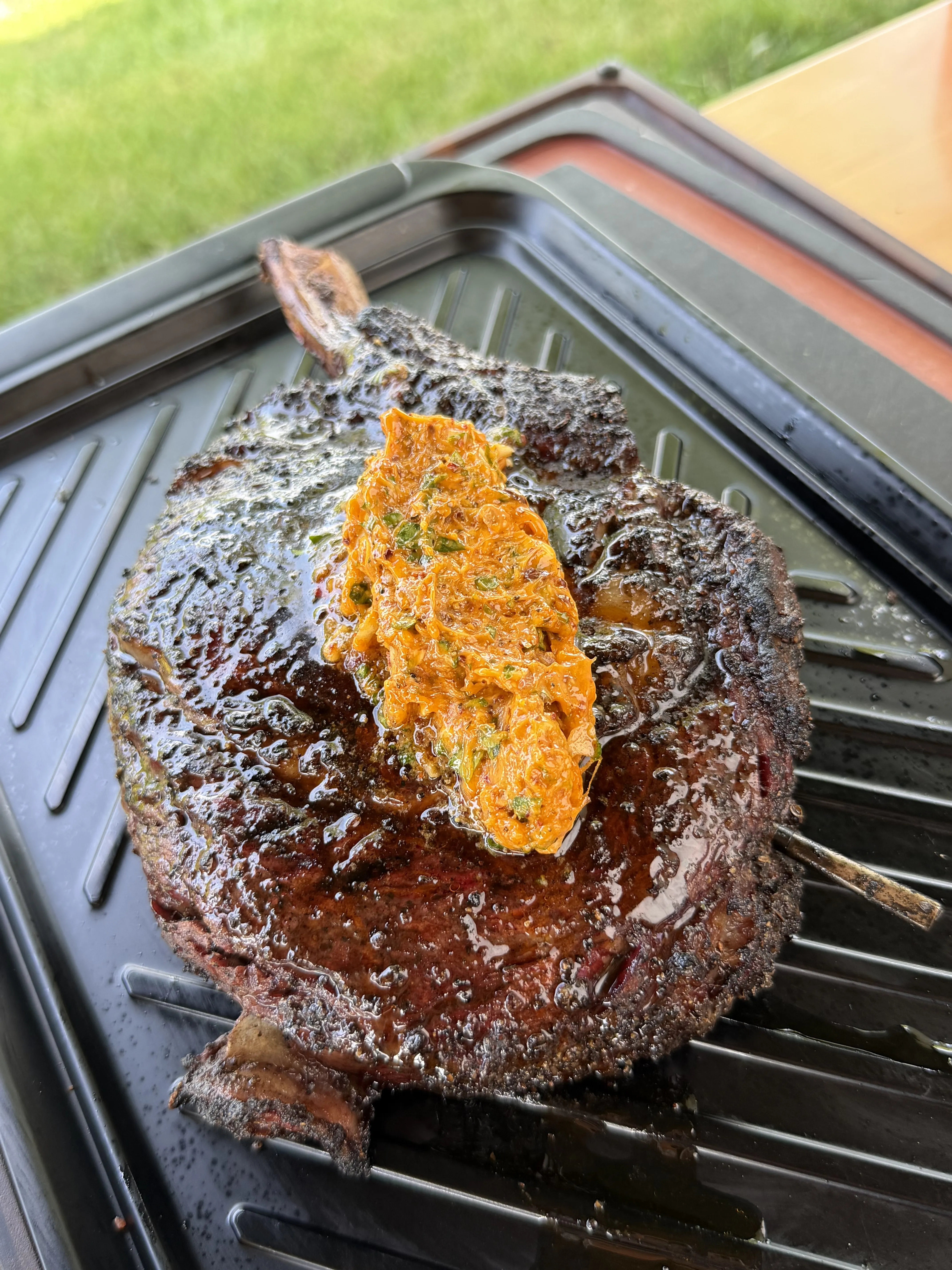 Thick tomahawk ribeye on the grill with chili butter melting over the top