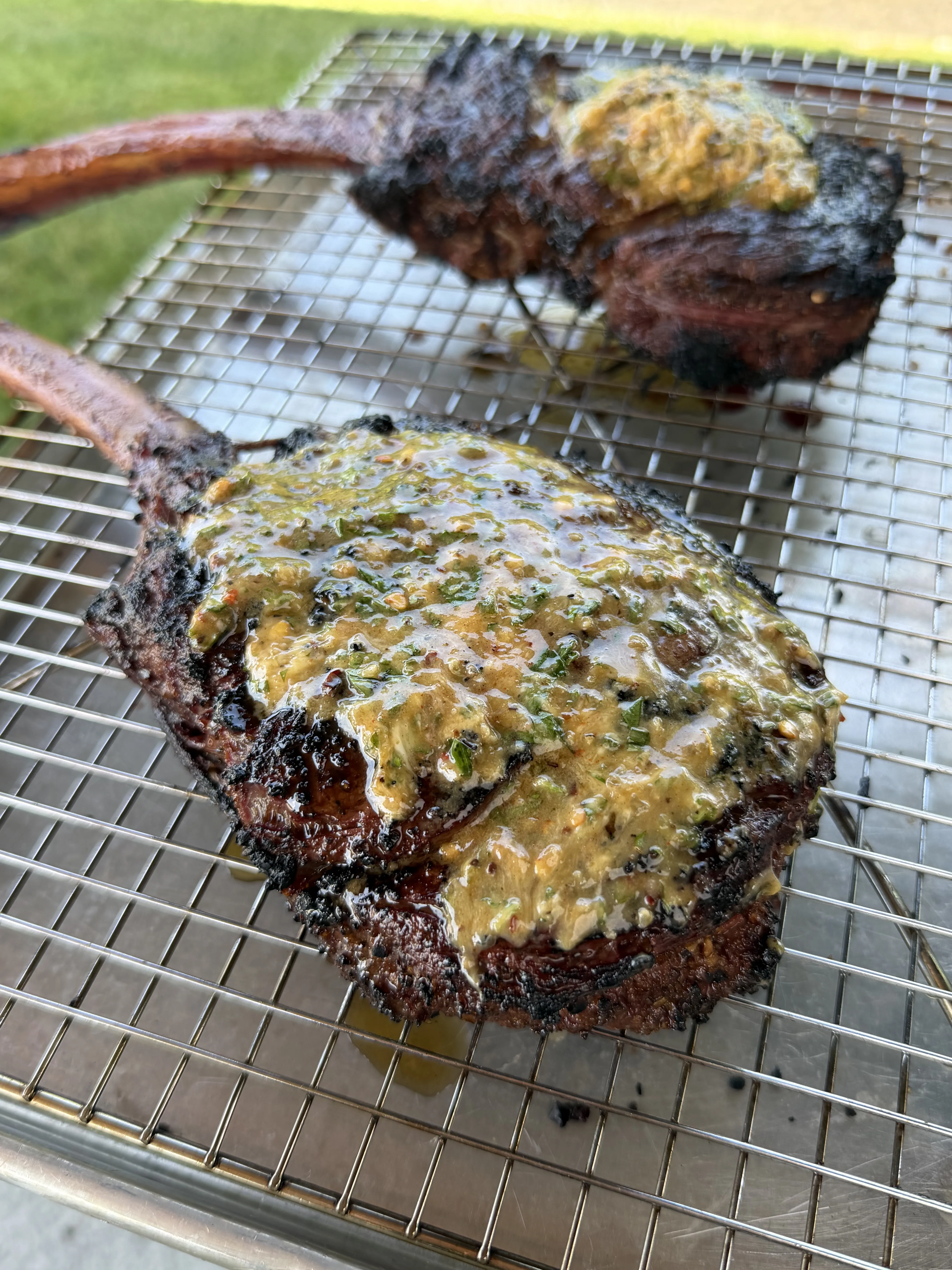 Rested tomahawk steaks on a wire rack with compound butter melting over the crust