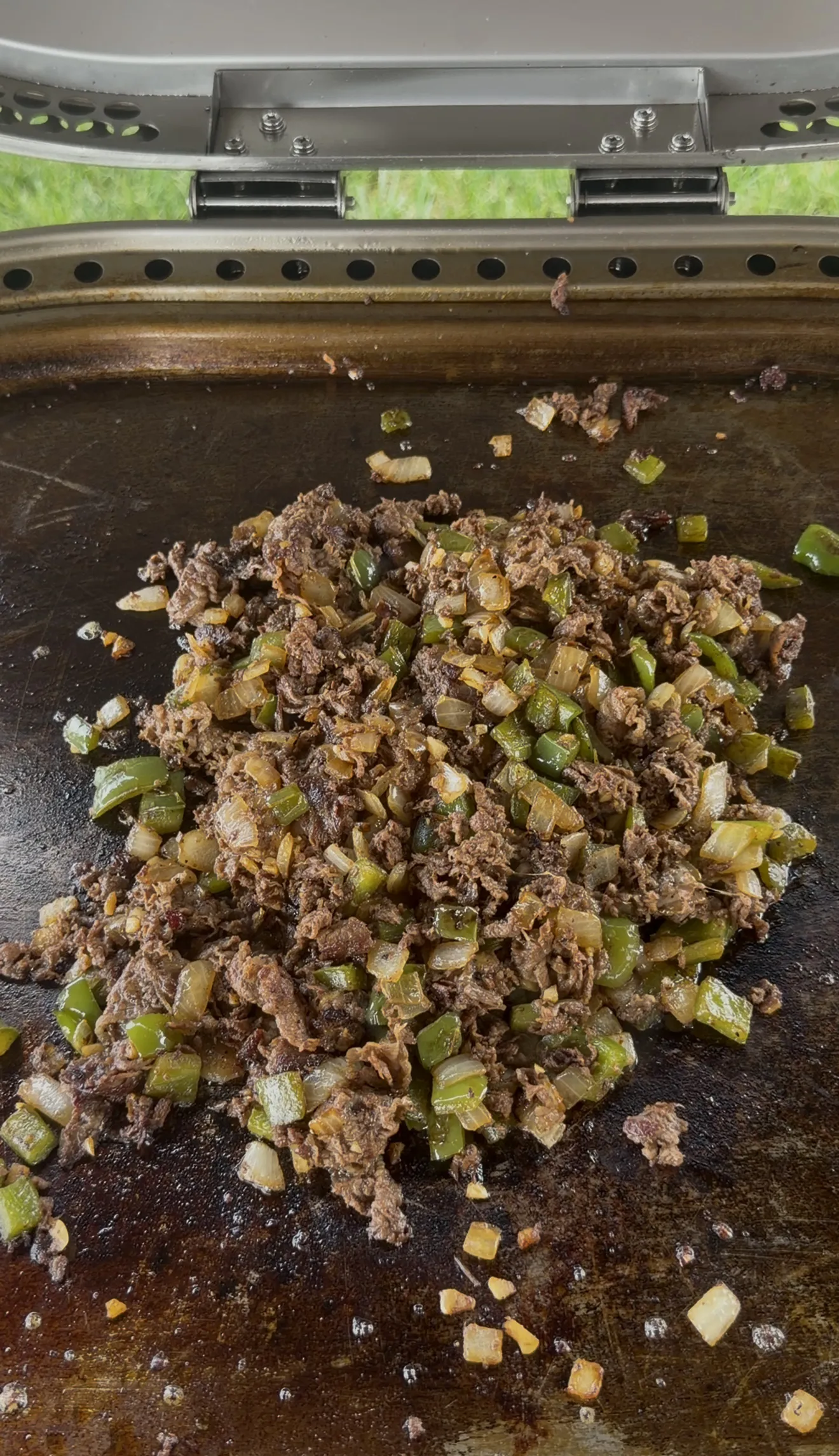 Chopped steak, green peppers, and onions cooking together on a flat top griddle