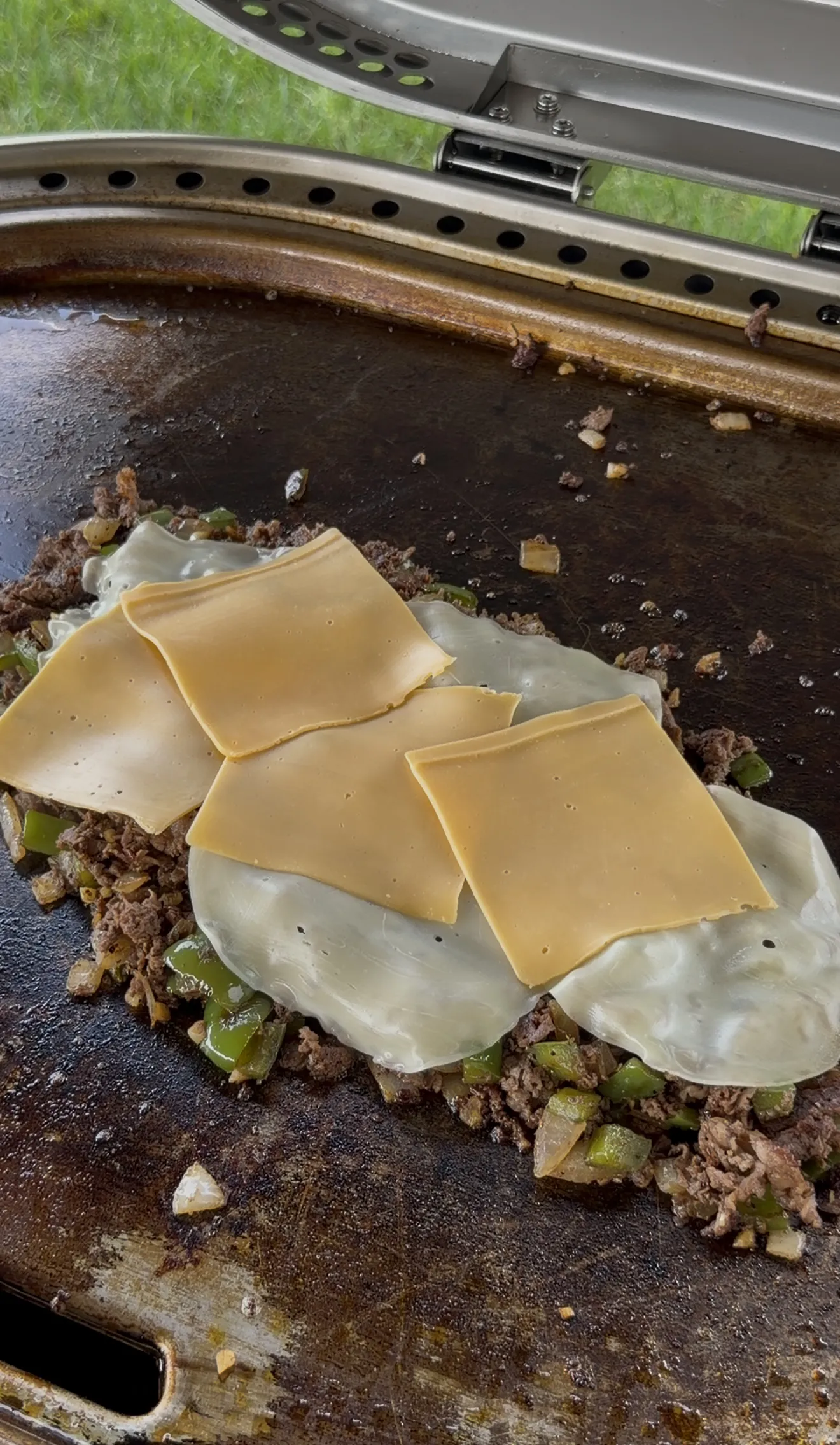 Provolone and American cheese melting over the cheesesteak filling on the griddle