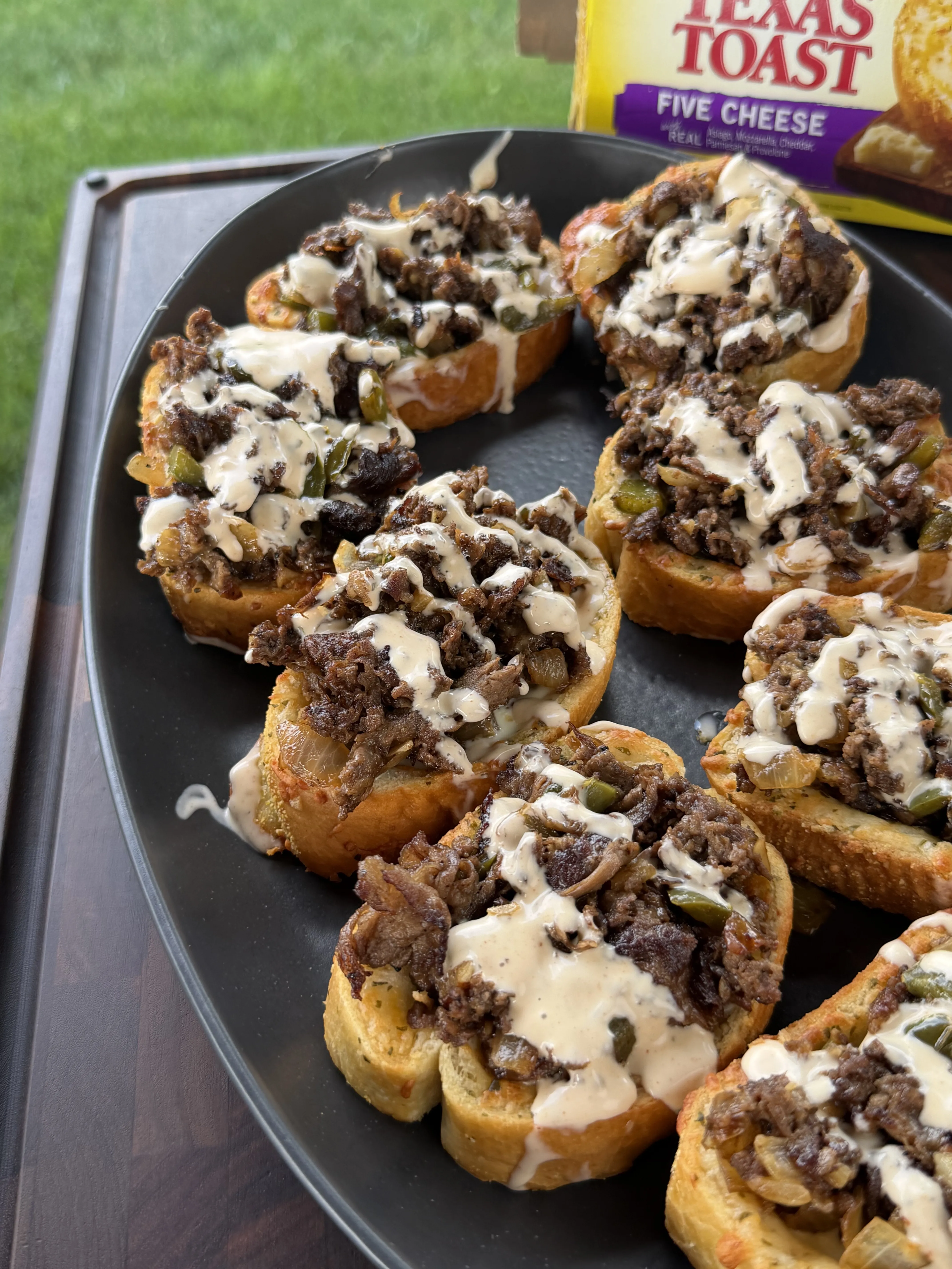 Cheesesteak Texas Toast topped with seasoned steak, peppers, onions, and a creamy cheese drizzle
