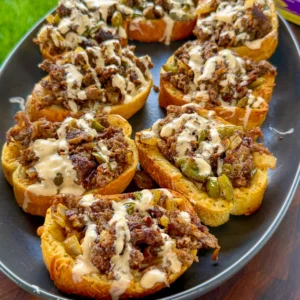 Philly cheesesteak Texas toast topped with seasoned beef, green peppers, onions, and creamy cheese sauce on a dark platter