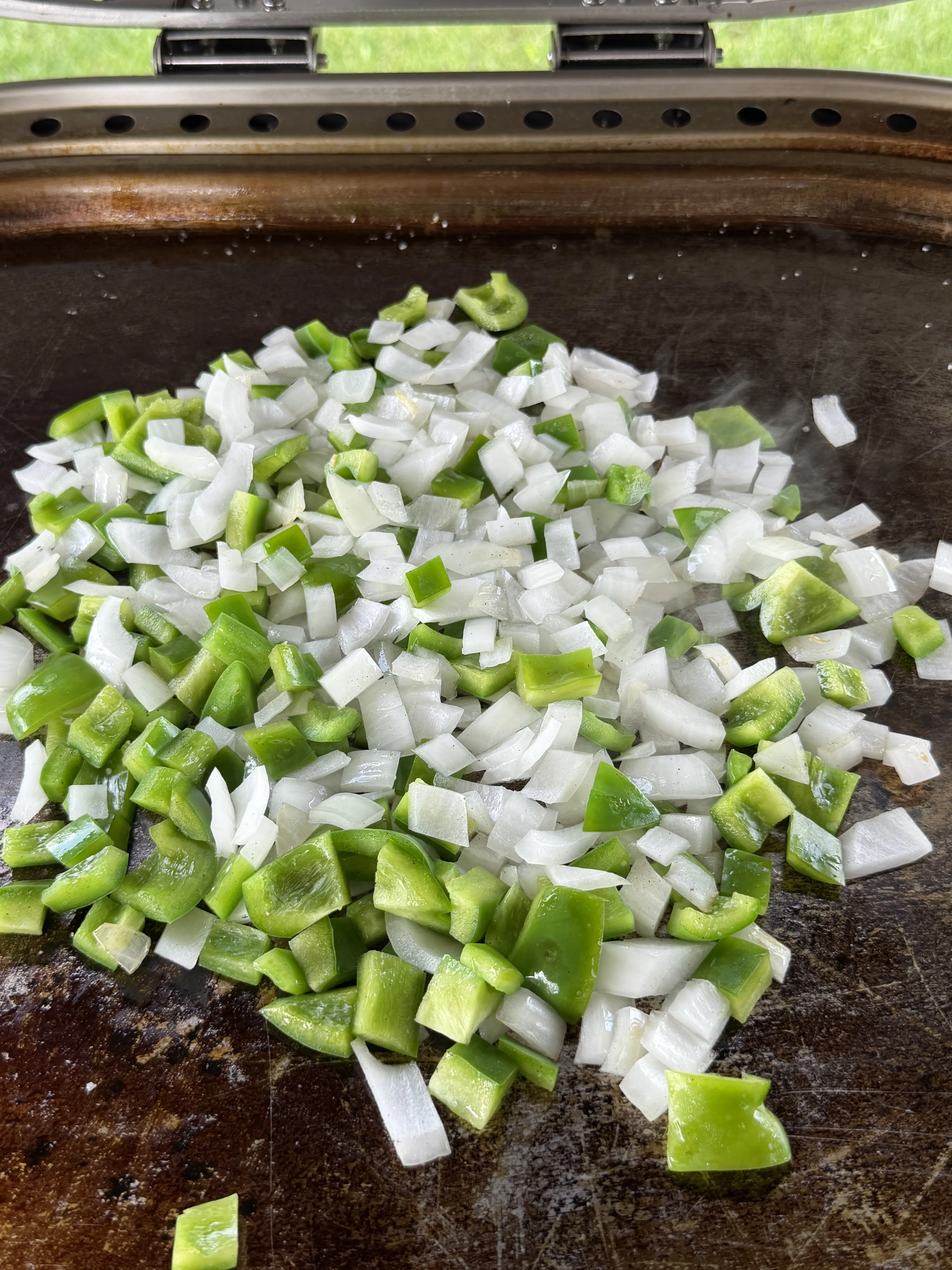 Green bell peppers and onions caramelizing on the flat top for cheesesteak Texas toast