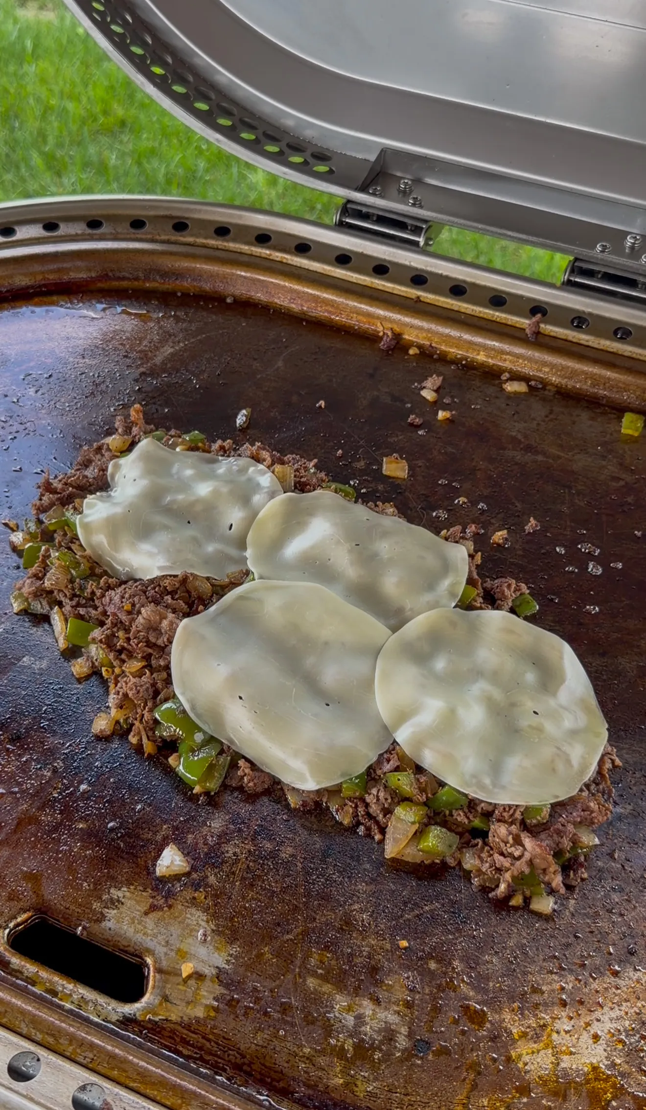 Provolone slices melting over chopped steak and green peppers on the griddle