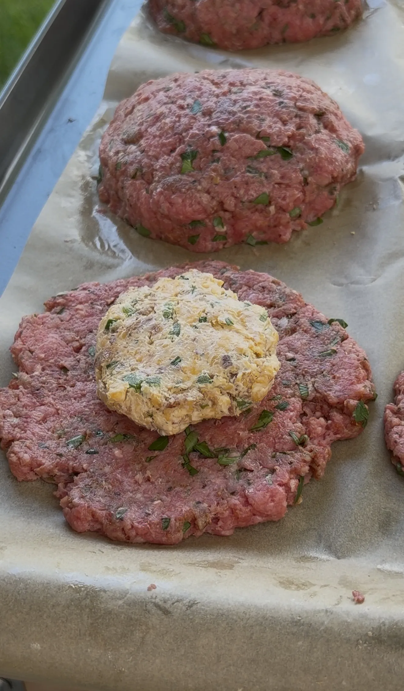 Raw burger patties on parchment with creamy bacon ranch stuffing mounded in the center