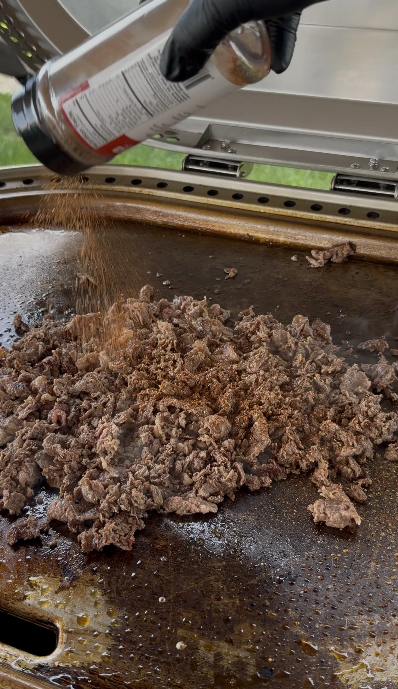 Seasoned shaved steak being sprinkled with spices on the flat top griddle