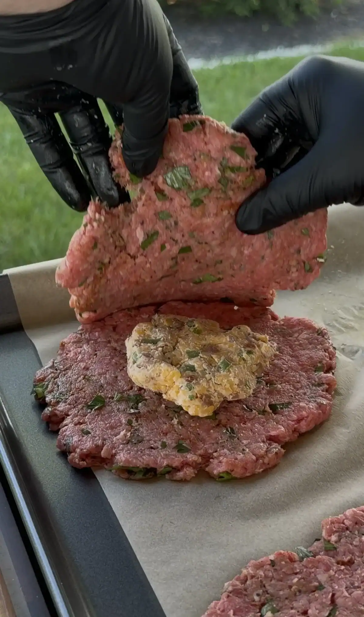 Gloved hands sealing a stuffed burger patty around the cheese filling on parchment