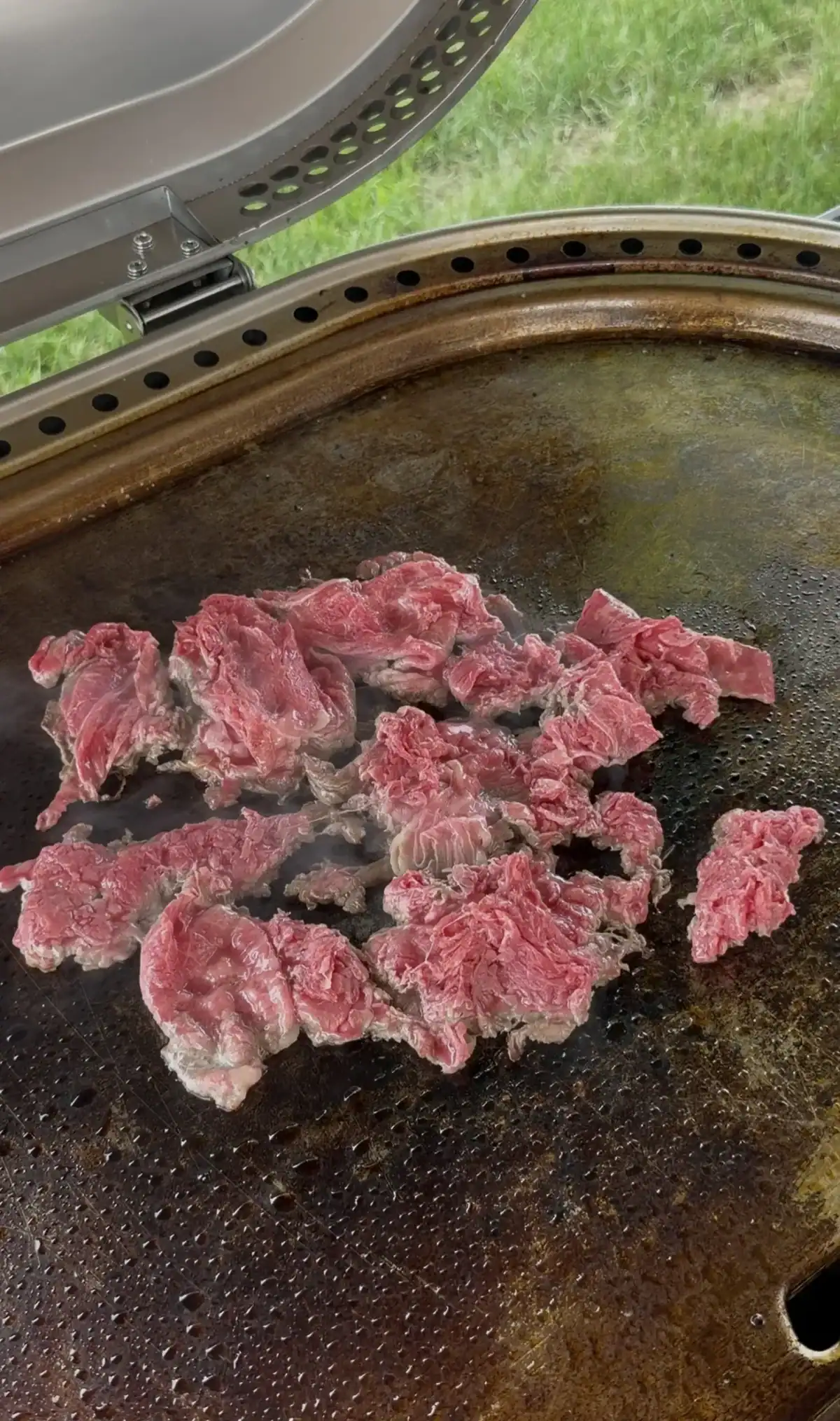 Thin slices of shaved ribeye cooking on a flat top griddle