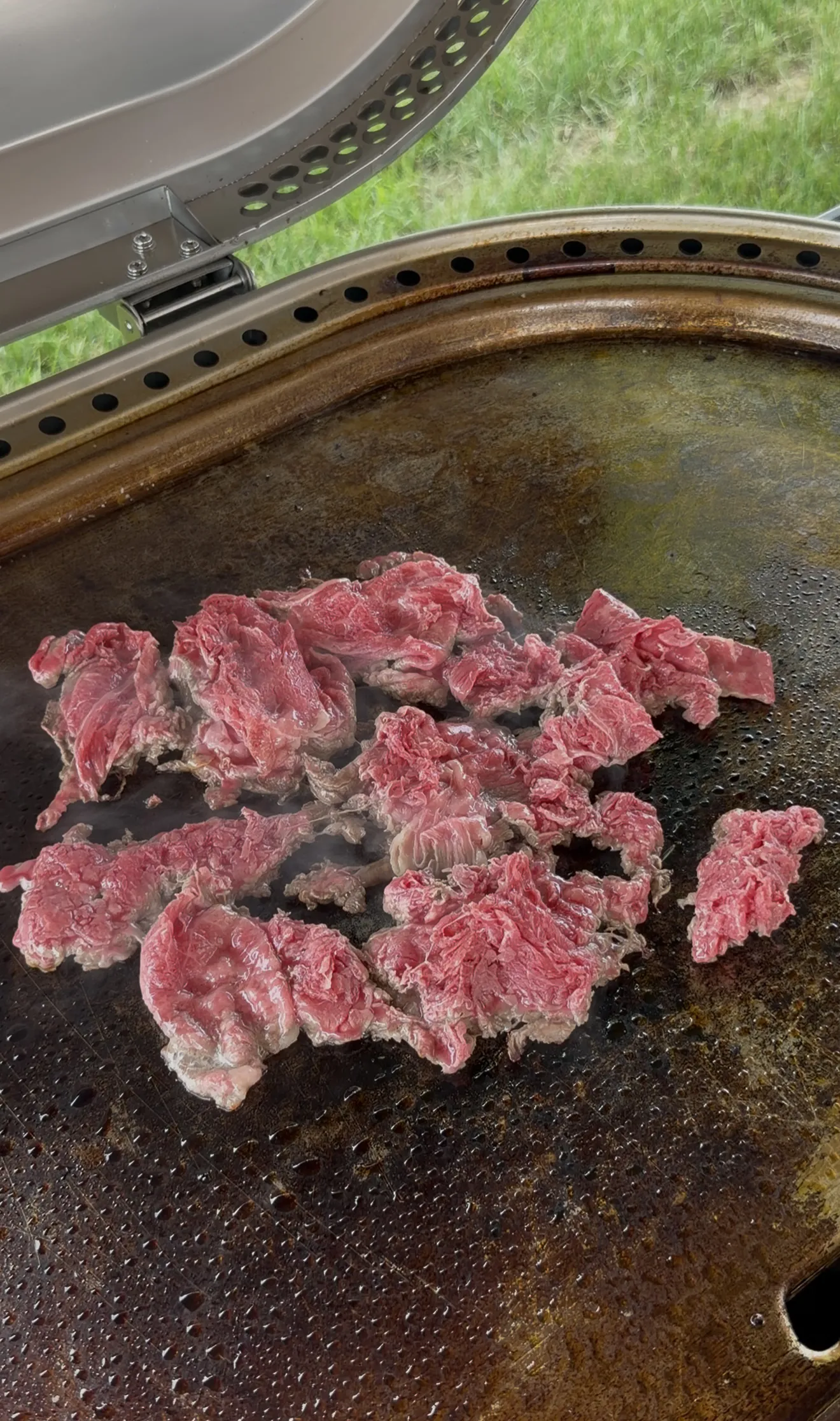 Thin slices of shaved ribeye cooking on a flat top griddle