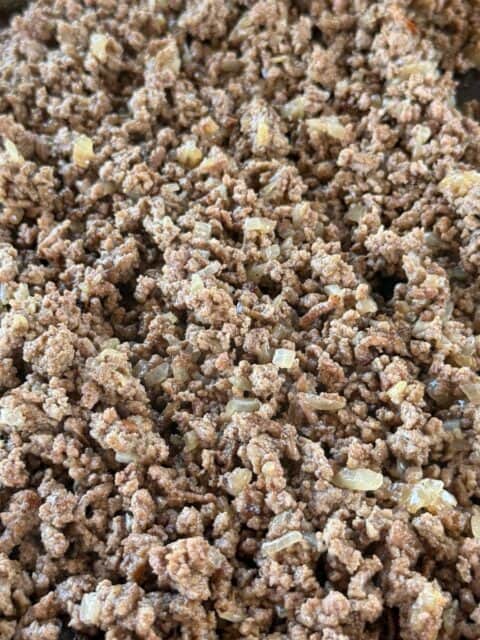 Browned ground beef with onions and jalapeños on the griddle for Bacon Cheeseburger Loaded Fries