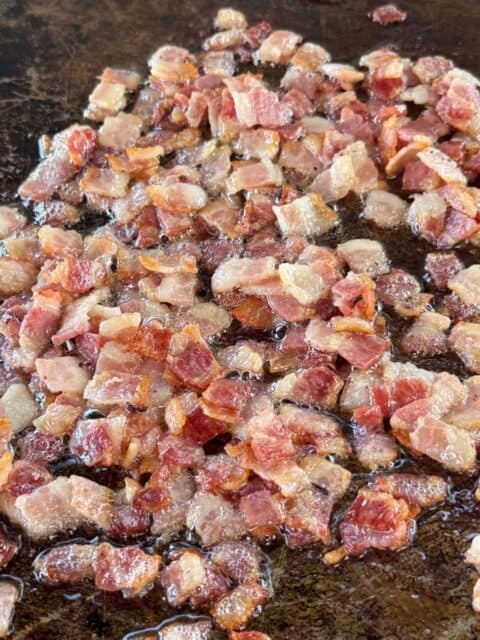Diced bacon cooking until crisp on a griddle for Bacon Cheeseburger Loaded Fries