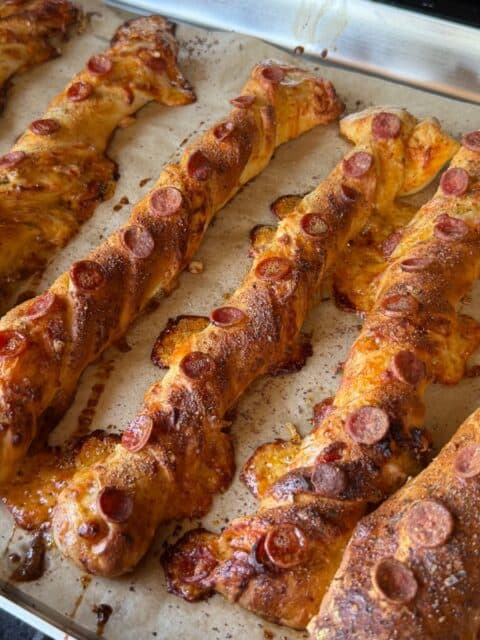 Pellet smoked pizza breadsticks browned on a parchment-lined sheet pan with crispy pepperoni edges