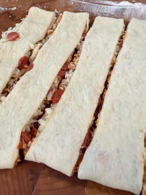 Folded pizza dough cut into 1-inch strips with cheese and pepperoni filling inside.