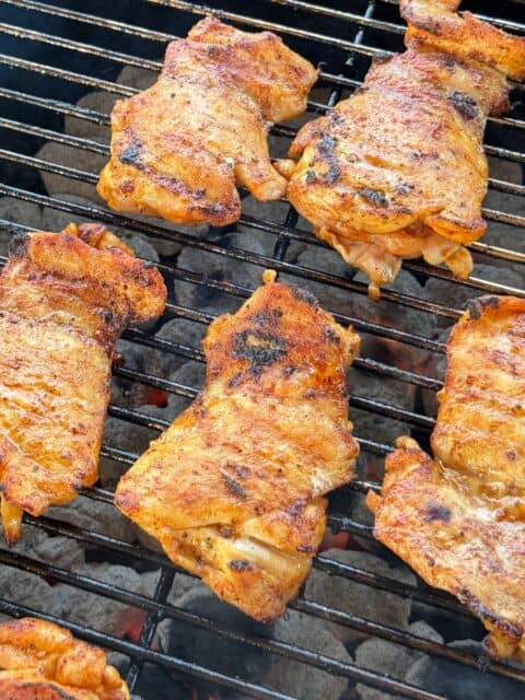 Seasoned chicken thighs grilling over charcoal for Mexican street corn pasta salad