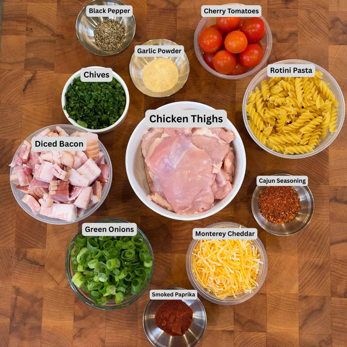 Ingredients for Chicken Bacon Ranch Pasta Salad including chicken thighs, rotini, bacon, Monterey cheddar, tomatoes, green onions, chives, and Cajun seasoning.
