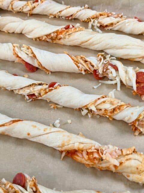 Pepperoni and cheese pizza breadsticks twisted and arranged on a parchment-lined baking sheet