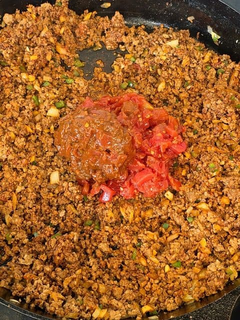 Fire-roasted diced tomatoes and tomato sauce added to ground beef and Mexican chorizo chili in a Dutch Oven.