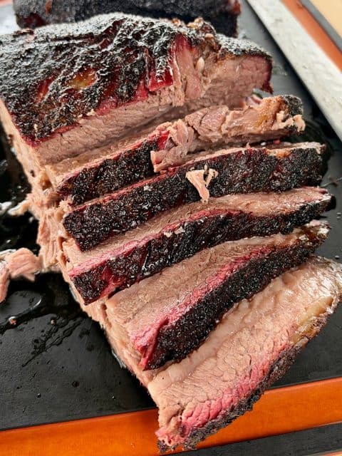 Texas-style smoked brisket sliced against the grain, showing tender beef, a pink smoke ring, and thick black pepper bark on each slice.