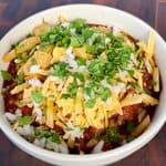 Smoked Over the Top Chili topped with shredded cheddar, diced white onion, cilantro, and corn chips.