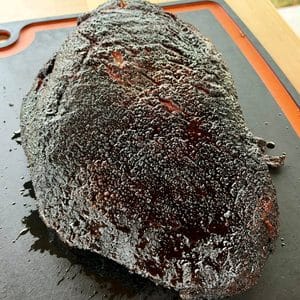 Whole Texas-style smoked beef brisket with a dark, coarse black pepper bark resting on a cutting board.