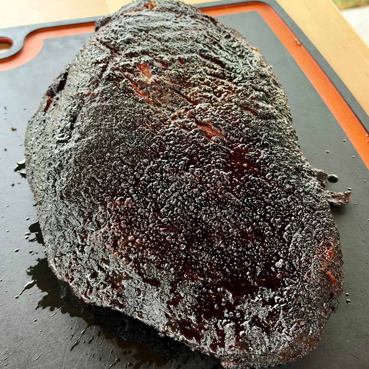 Whole Texas-style smoked beef brisket with a deep, dark peppery bark and rendered beef tallow resting on a cutting board.