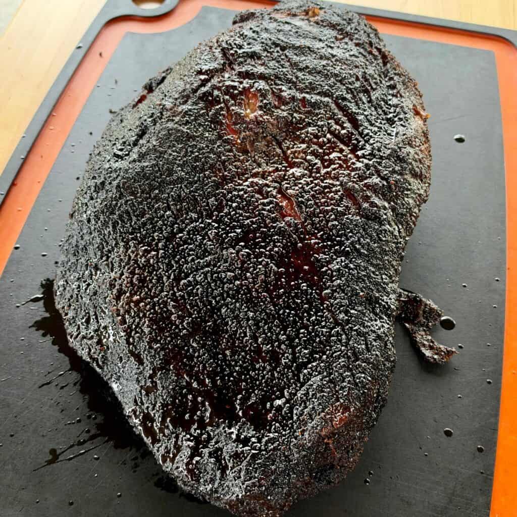 Whole Texas-style smoked beef brisket with a dark, peppery bark resting on a cutting board.