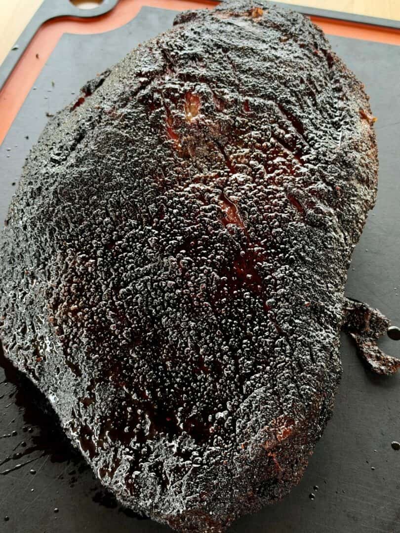 Whole Texas-style smoked beef brisket with a dark, peppery bark resting on a cutting board.