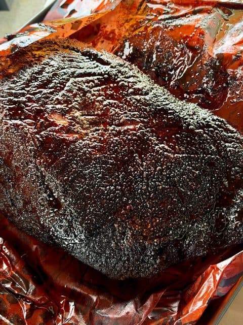 Whole smoked beef brisket with a deep, dark peppery bark and rendered juices after cooking until probe tender at 250°F.