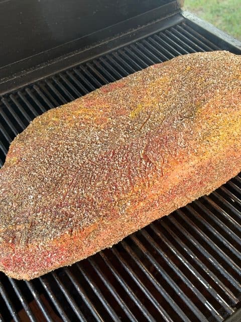 Whole packer beef brisket seasoned with kosher salt and coarse black pepper placed on charcoal smoker grates for low-and-slow smoking at 225°F.
